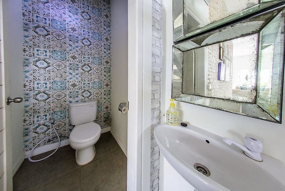 A cozy bathroom with vibrant blue patterned tiles, a white sink under a decorative mirror, and a toilet with a bidet hose, ideal for travelers seeking unique and functional accommodations.