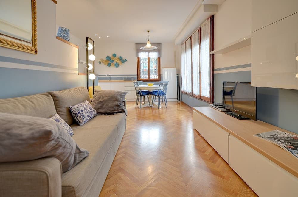 A cozy apartment living space features a plush sofa, modern dining area, and sleek entertainment unit, creating an inviting atmosphere ideal for travelers seeking comfort and style in urban accommodations.