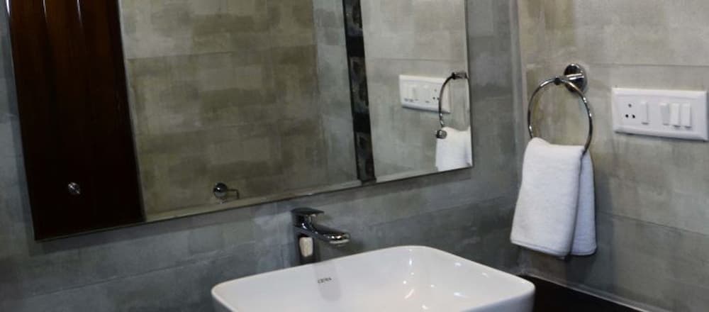 A modern bathroom with sleek gray tiled walls, a white sink, a large mirror, and a neatly hung towel exudes a clean and minimalist vibe, ideal for travelers seeking comfort and style in their accommodations.