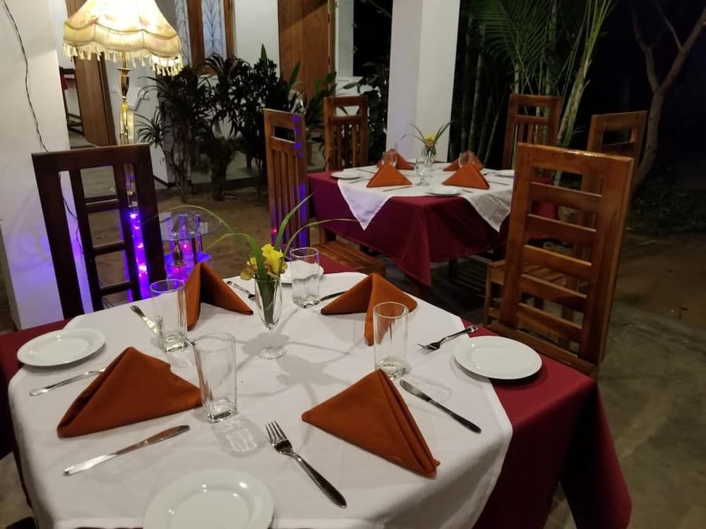 An inviting outdoor dining area at night features tables set with white linens, orange napkins, and floral centerpieces, surrounded by wooden chairs and ambient lighting, perfect for a romantic dinner or intimate gathering.