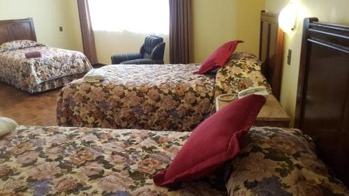 A cozy hotel room with floral-patterned beds, warm lighting, and a comfortable armchair creates an inviting atmosphere ideal for travelers seeking relaxation.
