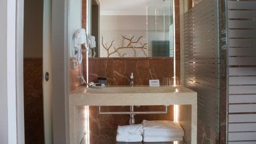 A modern hotel bathroom features a sleek marble sink, illuminated under-cabinet lighting, neatly folded towels, and a glass shower enclosure, creating a luxurious and inviting atmosphere ideal for travelers seeking comfort and style.