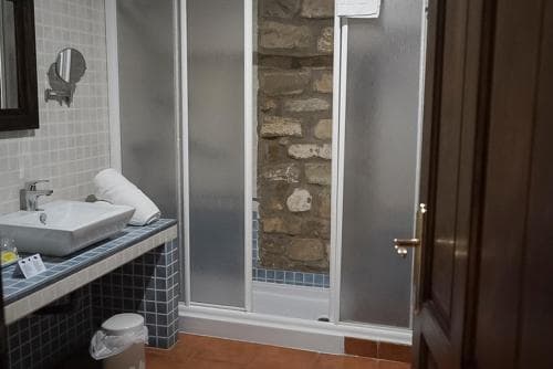 A cozy hotel bathroom features a modern sink, tiled countertop, and a glass-enclosed shower with a rustic stone wall, ideal for travelers seeking comfort and charm.