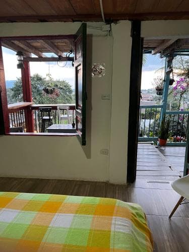 A cozy bedroom with a vibrant plaid bedspread opens to a serene balcony overlooking lush greenery, ideal for travelers seeking relaxation in a tranquil retreat.