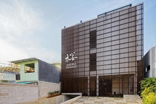 A modern, minimalist building with vertical slats and the sign "Sakura Terrace" stands prominently in an urban setting, evoking a serene and stylish atmosphere ideal for travelers seeking a contemporary accommodation experience.