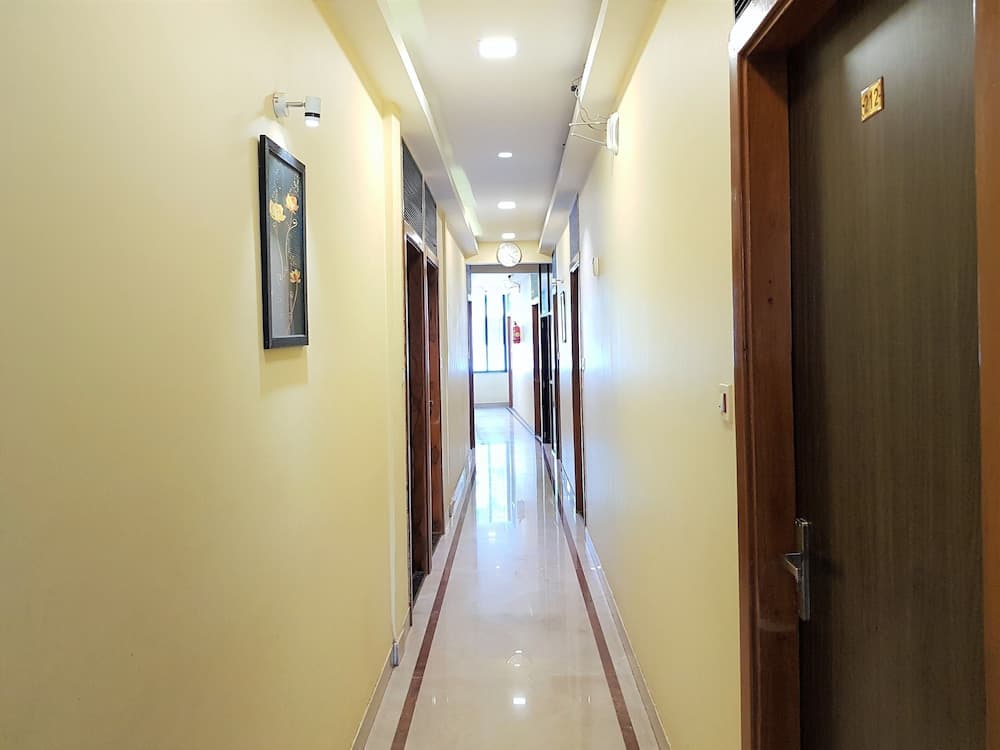 A warmly lit hotel corridor with yellow walls, framed artwork, wooden doors, and a polished floor creates an inviting atmosphere ideal for travelers seeking comfortable accommodations.