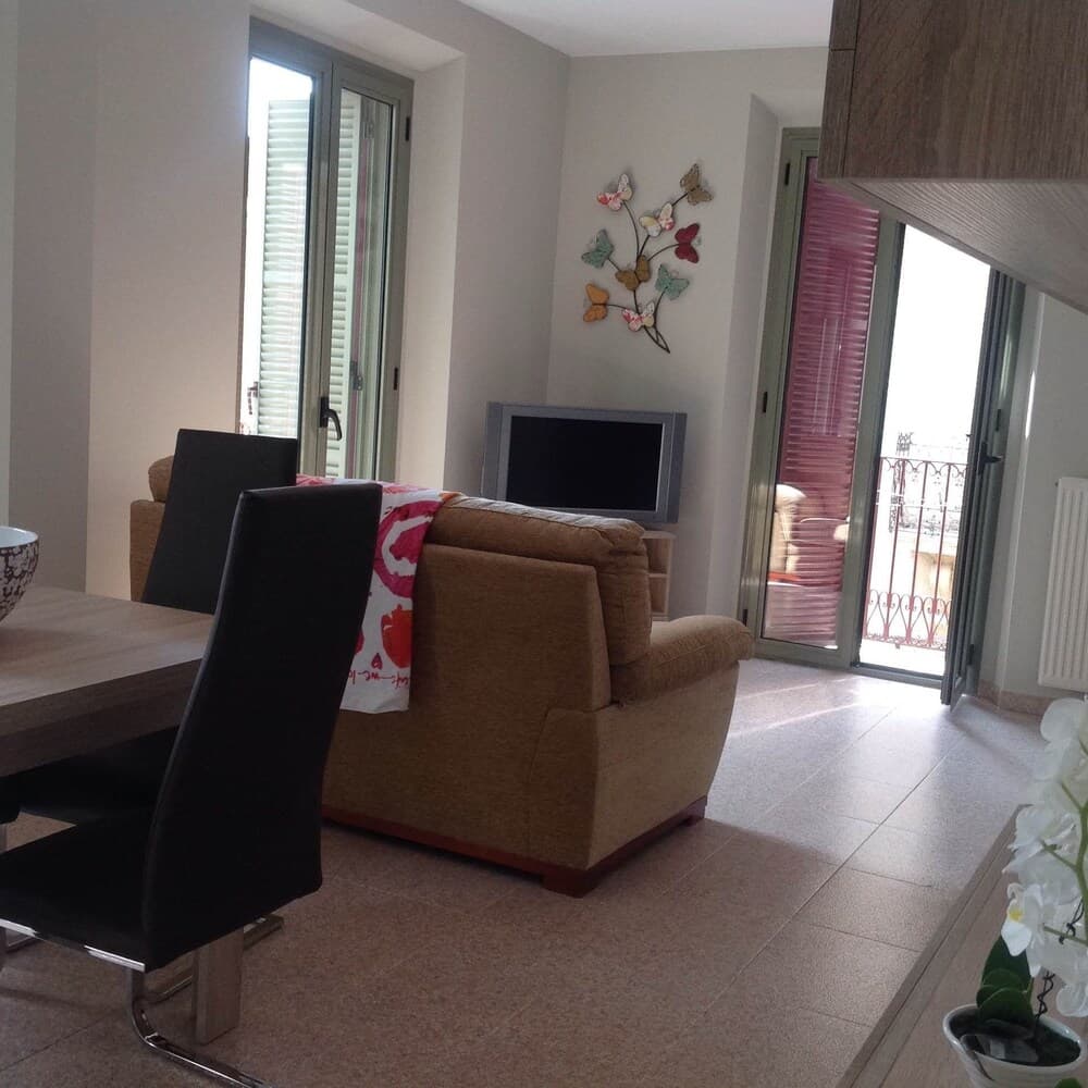 A cozy living room with a beige armchair, butterfly wall art, and sliding doors leading to a balcony offers a serene retreat for travelers seeking comfort in a vacation rental.