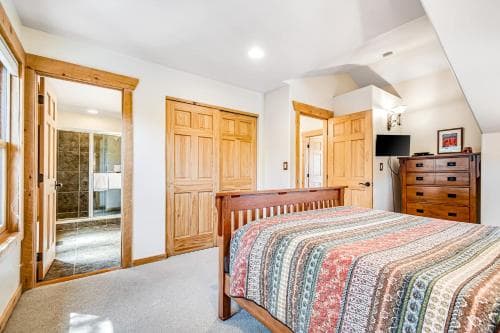 A cozy attic bedroom with wooden furnishings, a colorful striped bedspread, and an en-suite bathroom, ideal for a serene getaway retreat.