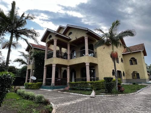 A luxurious two-story villa with a balcony and palm trees exudes tranquility in a tropical setting, ideal for a serene vacation retreat.