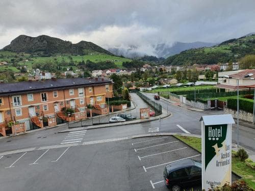 A serene view of a quaint town nestled among lush green hills under a cloudy sky, featuring a hotel sign and parked cars in the foreground, ideal for travelers seeking a peaceful retreat in a picturesque rural setting.