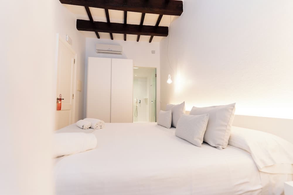 A cozy bedroom with white linens, wooden beams, and soft lighting creates a serene atmosphere ideal for travelers seeking relaxation in a boutique hotel setting.