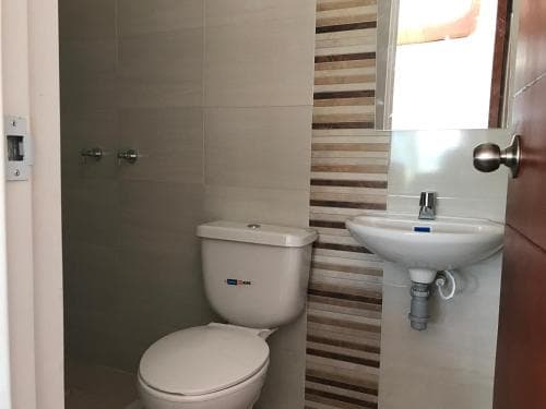 A compact bathroom with beige tiles, a white toilet, and a sink under a mirror exudes a clean and functional vibe, ideal for travelers seeking basic amenities in a guesthouse or hotel setting.
