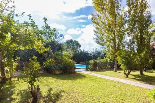 A serene garden path lined with lush greenery leads to a tranquil pool area under a partly cloudy sky, ideal for a relaxing vacation retreat.