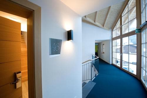 A cozy, modern hallway with wooden accents, a blue carpeted staircase, and large windows offering a bright, inviting atmosphere ideal for a comfortable stay in a boutique hotel or guesthouse.