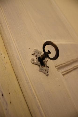 A vintage key rests elegantly in an ornate lock on a softly lit wooden door, evoking a nostalgic atmosphere ideal for exploring historic homes or antique shops.