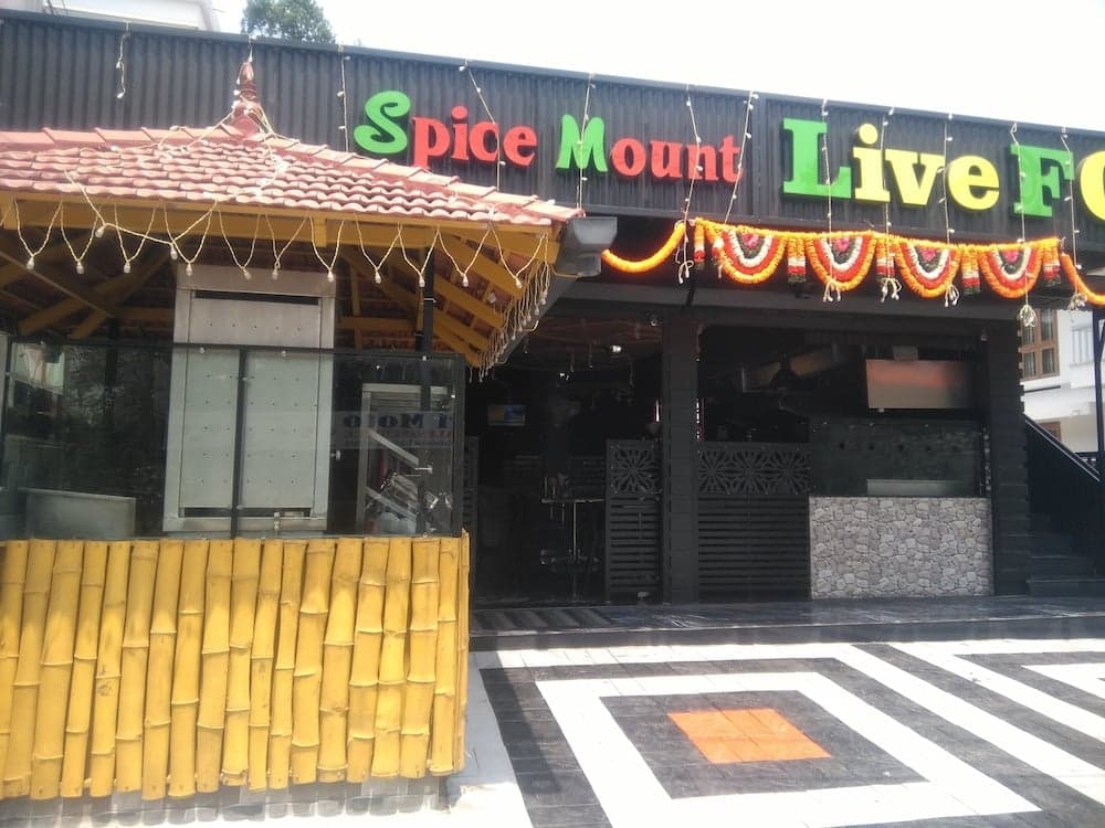 A vibrant restaurant entrance adorned with colorful garlands and a traditional tiled roof invites travelers to explore its live food offerings in a festive and inviting atmosphere.