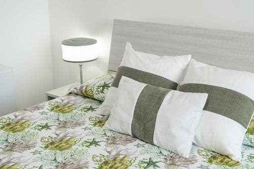 A cozy bedroom scene featuring a neatly made bed with a coral-themed duvet, soft pillows, and a modern bedside lamp, ideal for travelers seeking a tranquil and stylish accommodation experience.