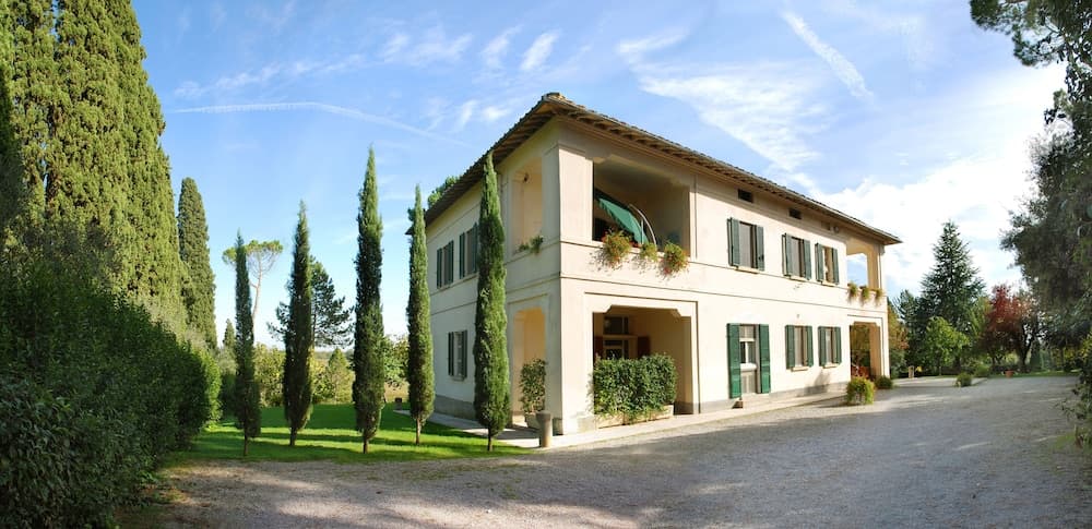 A serene Tuscan villa with lush greenery and tall cypress trees under a bright blue sky, ideal for a tranquil countryside retreat.