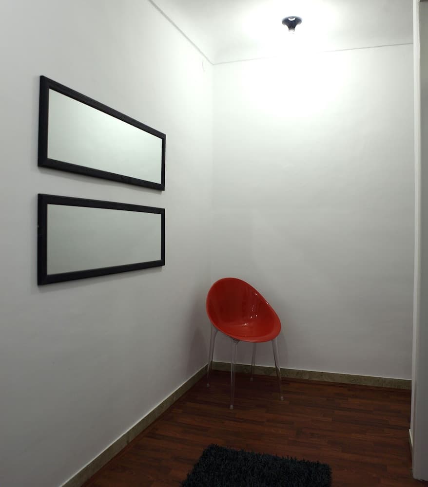 A minimalist indoor space features a vibrant red chair against white walls adorned with two black-framed mirrors, creating a serene and modern atmosphere ideal for travelers seeking a quiet retreat or art enthusiasts exploring contemporary design.
