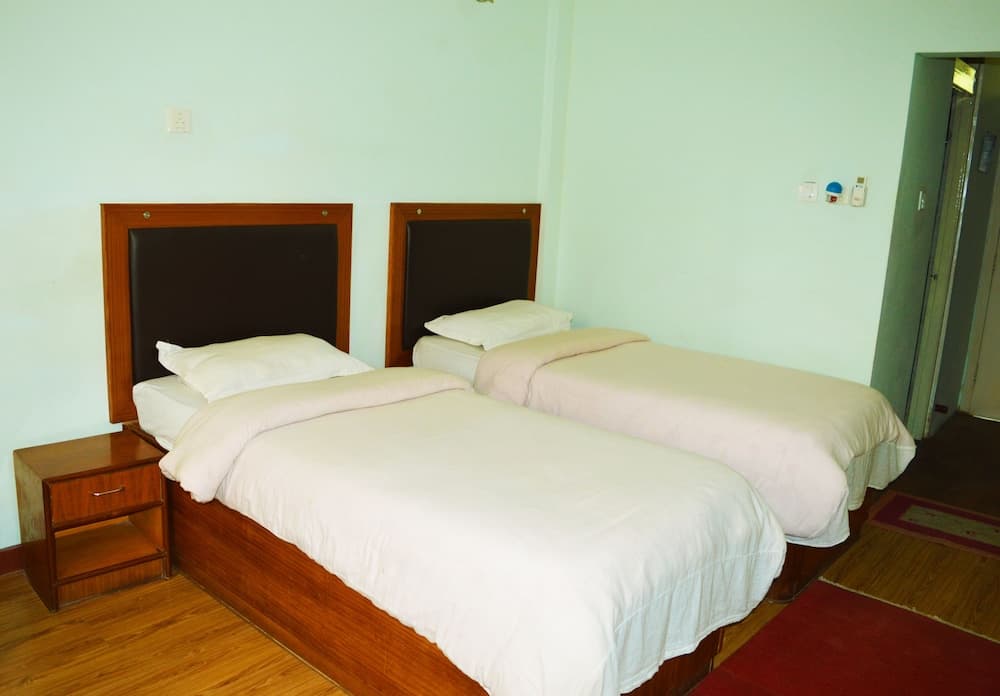 A cozy hotel room features two neatly made beds with white linens, wooden headboards, and a small bedside table, creating a simple and inviting atmosphere ideal for budget travelers seeking comfort.