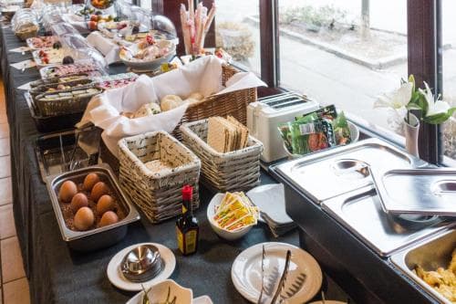 A cozy indoor buffet setup featuring fresh bread in woven baskets, eggs, condiments, and a warm serving station, ideal for travelers seeking a welcoming breakfast experience.