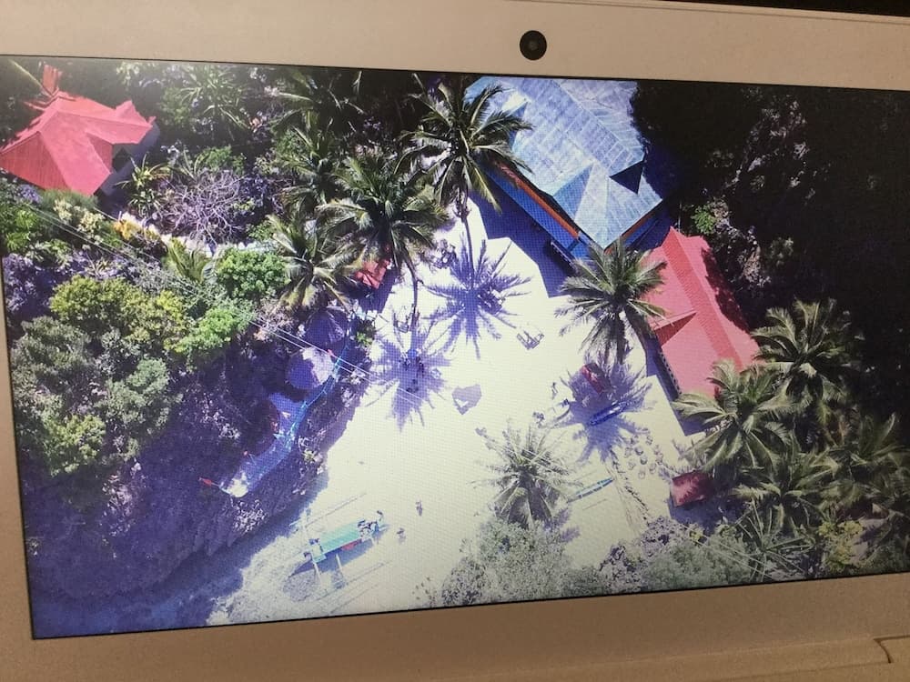 An aerial view of a vibrant tropical resort with lush greenery, palm trees, colorful roofs, and serene pathways evokes a tranquil vacation atmosphere, ideal for travelers seeking relaxation and natural beauty.