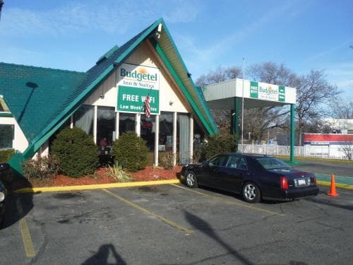 A cozy motel with a green roof and "Budgetel" signage offers free Wi-Fi in a sunny parking lot setting, ideal for travelers seeking budget-friendly accommodations.