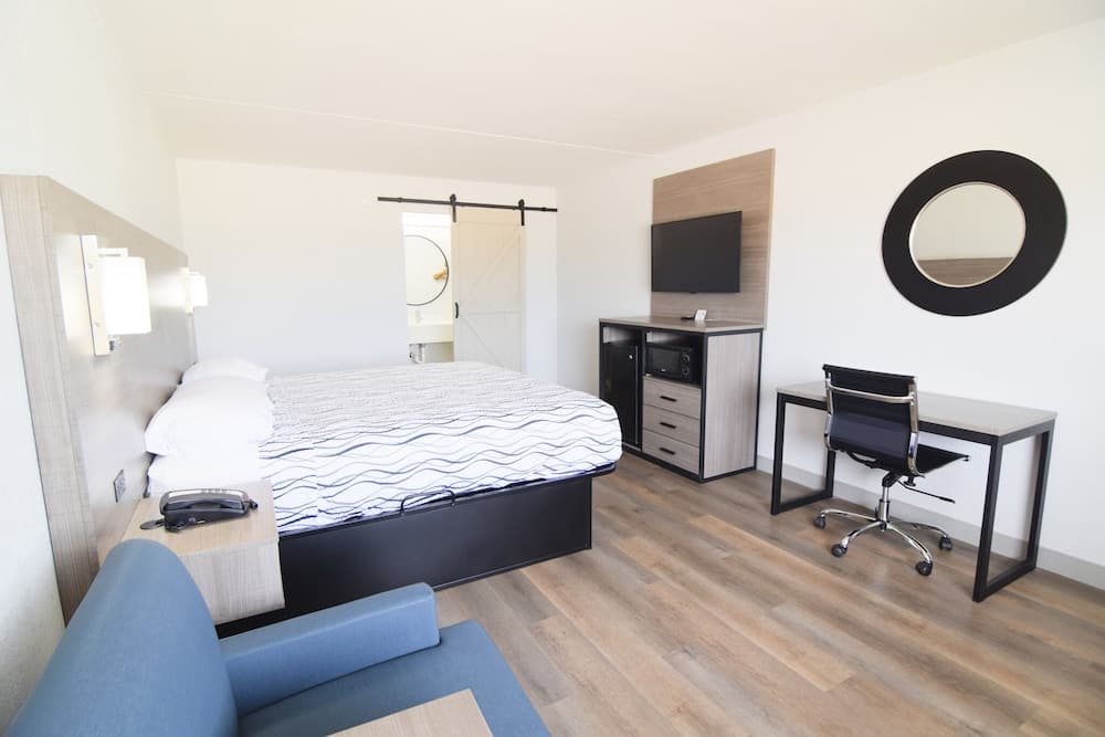 A cozy hotel room features a neatly made bed, modern desk setup, and stylish blue armchair, creating a welcoming atmosphere ideal for travelers seeking comfort and functionality.