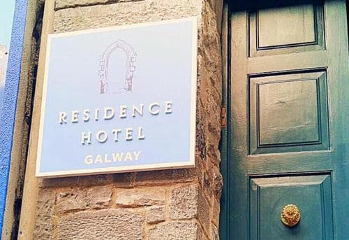 A charming stone facade with a sign reading "Residence Hotel Galway" beside a teal wooden door evokes a cozy, inviting atmosphere ideal for travelers seeking a quaint European getaway.