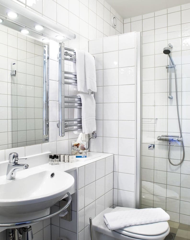 A clean, modern bathroom with white tiled walls, a sink, shower, heated towel rack, and neatly arranged toiletries creates a serene and functional space ideal for travelers seeking comfort and hygiene.