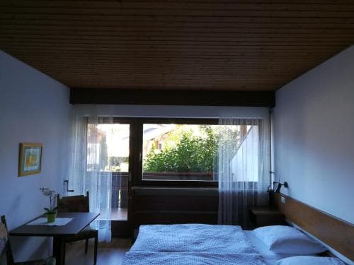 A cozy hotel room with a neatly made bed, wooden ceiling, and a balcony view of lush greenery, ideal for travelers seeking relaxation in a serene environment.