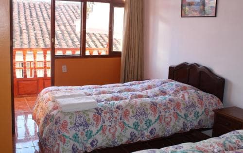 A cozy hotel room with a floral-patterned bedspread overlooks a charming balcony with terracotta tiles, ideal for travelers seeking a peaceful retreat in a traditional setting.