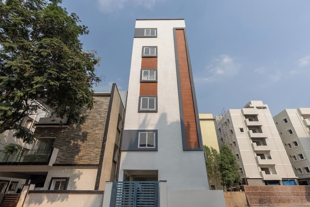 A modern residential building with a sleek design and orange accents stands under a clear blue sky, surrounded by lush green trees, ideal for urban living and property investment.