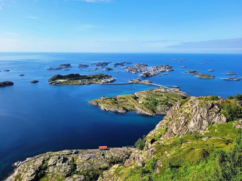 A breathtaking panoramic view of scattered islands and turquoise waters under a clear blue sky, ideal for nature enthusiasts exploring the scenic coastal landscapes of Norway.
