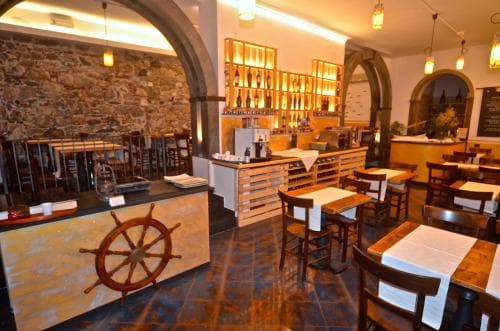 A cozy restaurant interior with rustic stone walls, warm lighting, wooden furniture, and a decorative ship's wheel, ideal for travelers seeking a charming dining experience in a historic setting.