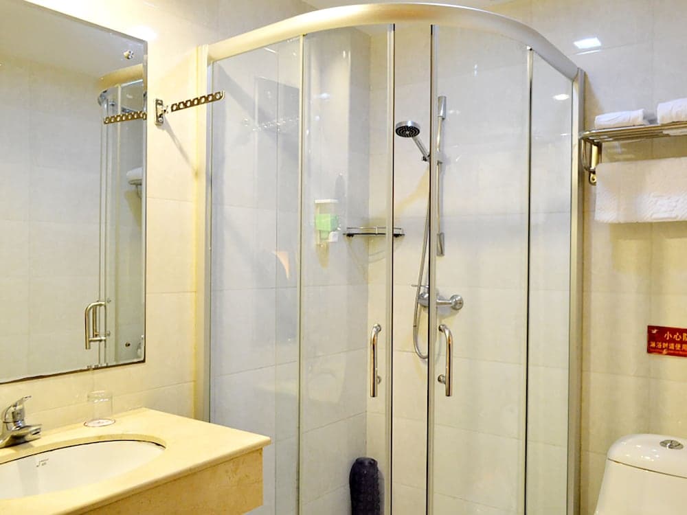 A clean and modern hotel bathroom features a glass-enclosed shower, a sink with a mirror, and neatly arranged towels, ideal for travelers seeking comfort and hygiene during their stay.