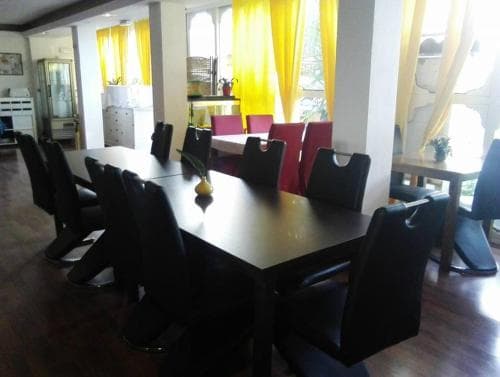 A cozy dining area with sleek black tables and chairs under bright yellow curtains, perfect for travelers seeking a warm and inviting space for group meals or gatherings.