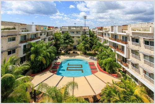 A vibrant tropical resort features a central pool surrounded by lush palm trees and multi-story buildings under a bright blue sky, ideal for a relaxing vacation getaway.