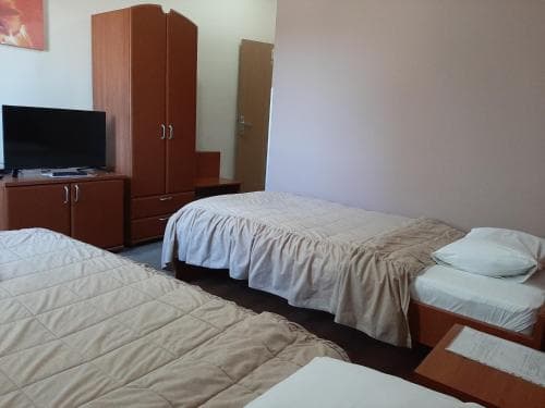A cozy budget hotel room features two neatly made beds, wooden furniture including a wardrobe and dresser, and a flat-screen TV, ideal for travelers seeking simple accommodations.
