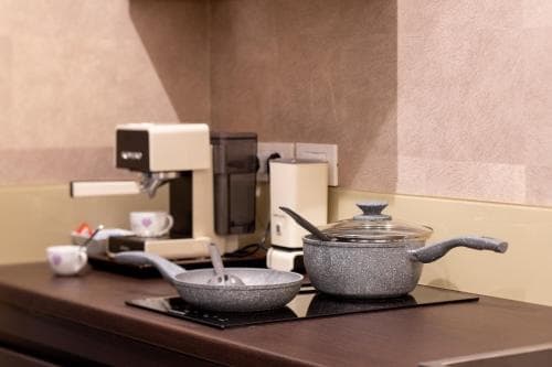 A cozy kitchenette setup featuring a coffee machine, cooking pots on an induction stove, and cups, ideal for travelers seeking convenience in a compact living space.