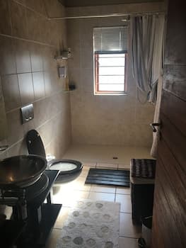 A cozy bathroom with beige tiles, a window with blinds, a shower curtain, and neatly folded towels creates a serene atmosphere, ideal for travelers seeking a clean and comfortable space to unwind.