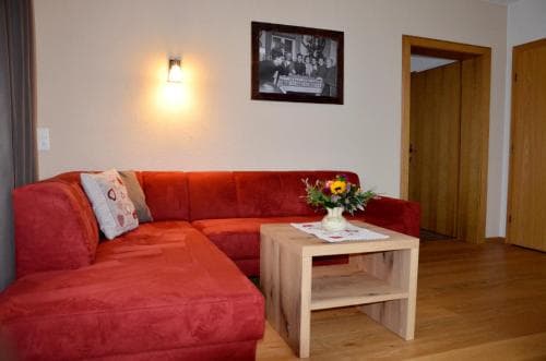 A cozy living room with a vibrant red sofa, wooden coffee table adorned with flowers, and warm lighting creates an inviting atmosphere, ideal for travelers seeking comfort in a vacation rental.