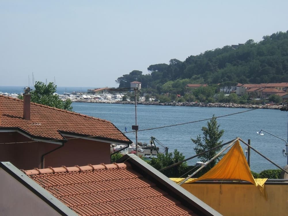 A serene coastal town view featuring terracotta rooftops, calm waters, docked boats, lush greenery, and a distant hilltop castle, ideal for travelers seeking a peaceful seaside retreat.