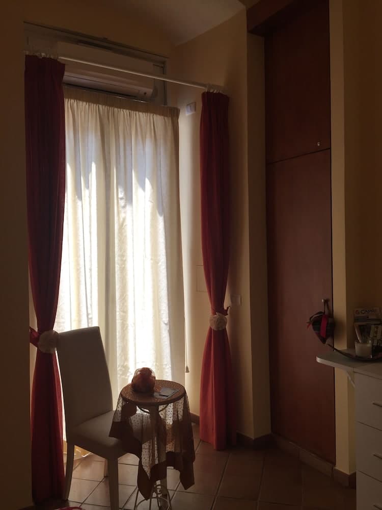 A cozy hotel room corner features soft sunlight filtering through sheer curtains, a small table draped in lace with a bag of bread, and a comfortable chair, ideal for a quiet morning retreat during a leisurely trip.
