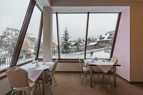 A cozy indoor dining area with large windows offers a serene view of a snowy village landscape, perfect for travelers seeking a tranquil winter retreat.