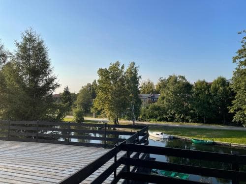 A serene lakeside deck offers a tranquil view of calm waters, docked boats, lush greenery, and distant buildings under a clear blue sky, ideal for peaceful retreats or nature photography.
