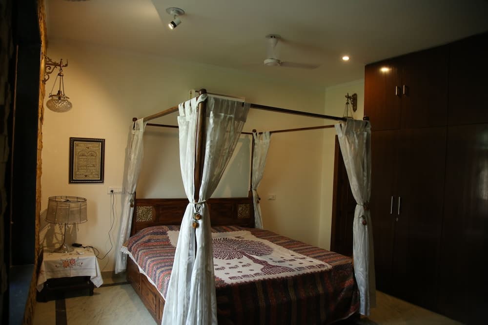 A cozy bedroom with a four-poster bed draped in white curtains, wooden furnishings, and soft lighting creates an inviting atmosphere ideal for travelers seeking a serene retreat.