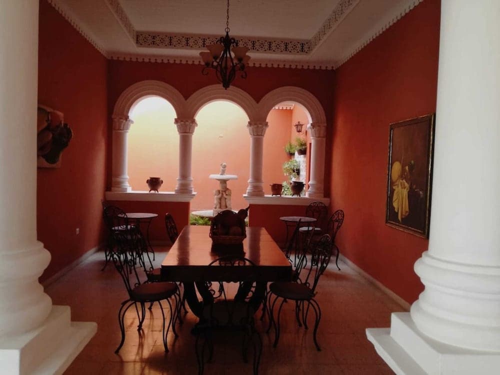 A cozy indoor dining area with vibrant red walls, white columns, arched windows, and elegant furniture creates an inviting atmosphere perfect for travelers seeking a charming and intimate restaurant experience.