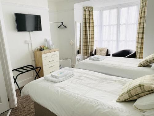 A cozy hotel room features two neatly made beds with plaid accents, a bright bay window, and modern amenities, ideal for travelers seeking comfort and relaxation.