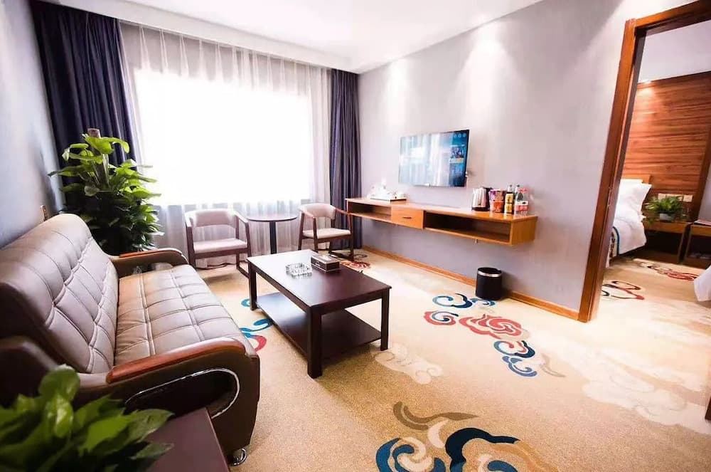 A cozy hotel suite features a plush sofa, vibrant carpet patterns, and a bright window, creating a welcoming atmosphere ideal for travelers seeking comfort and relaxation.